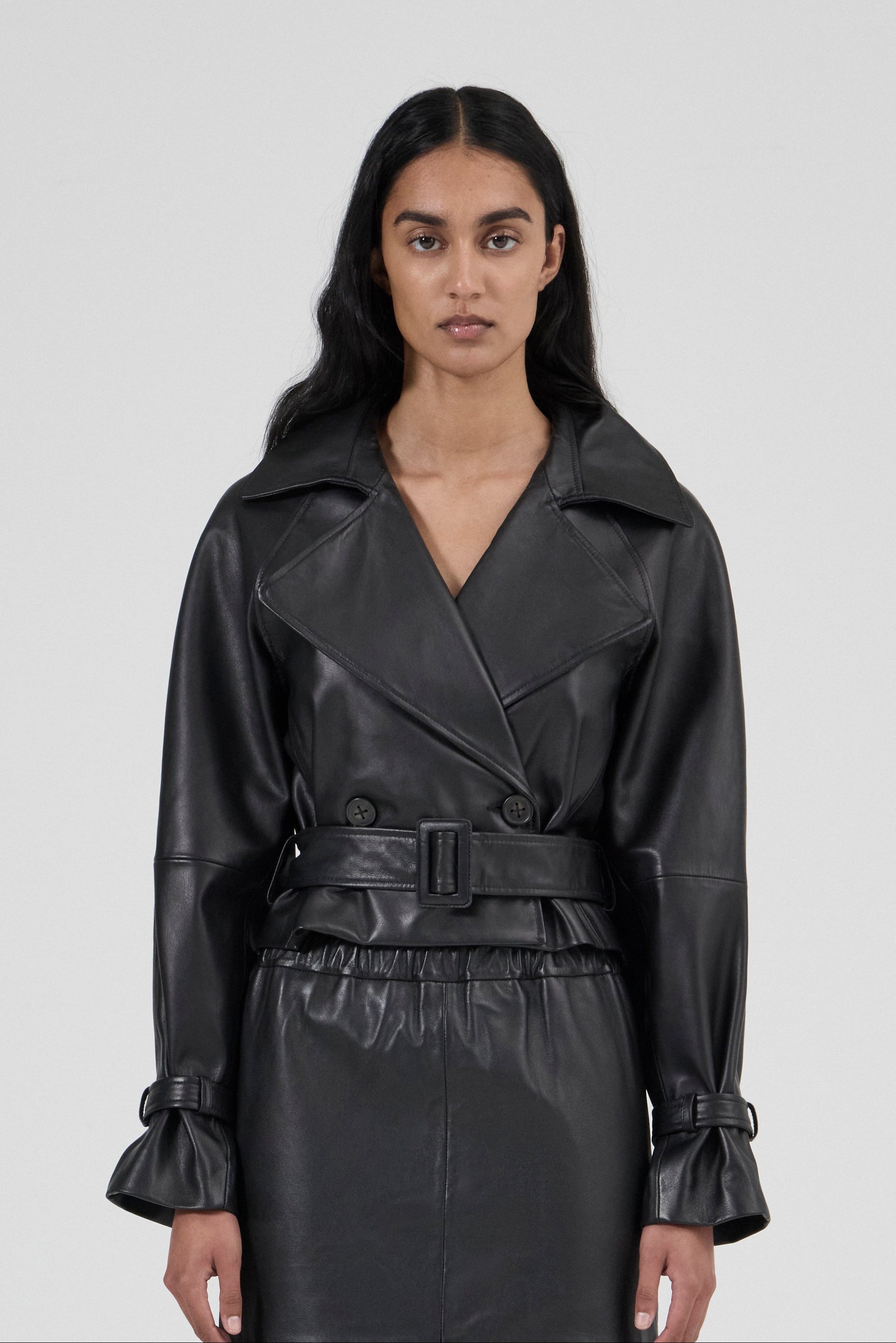 Woman wearing a black leather trench coat against a plain background